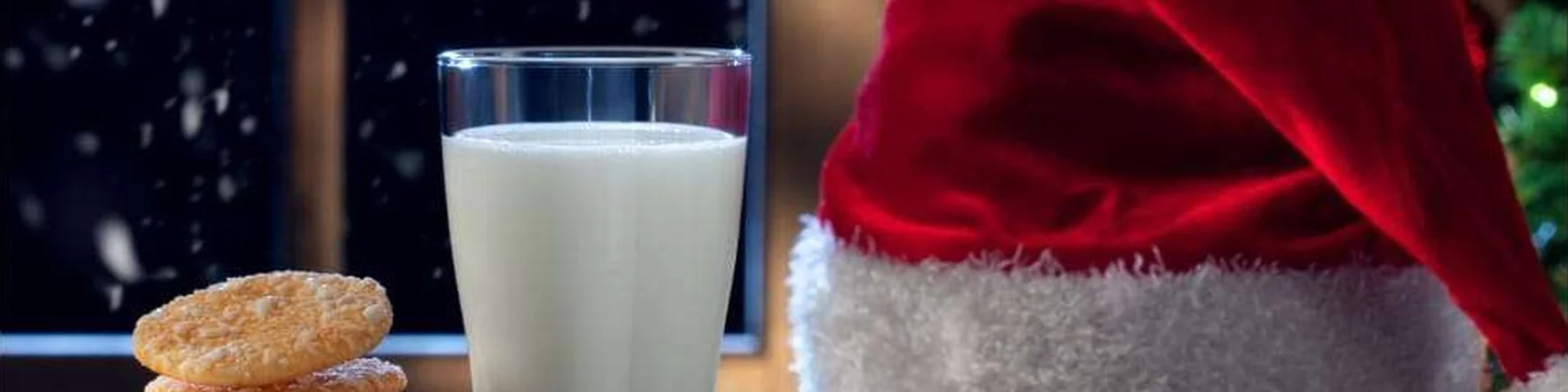 Cookies, a glass of milk and a Santa hat on a wooden table in a snowy window